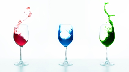 three wine glasses with splashing liquids in red, blue and gree